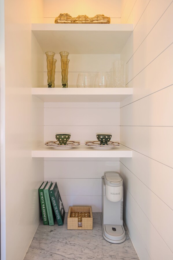 A kitchen with white shelves, two green books, a white coffee maker, and a woven basket.