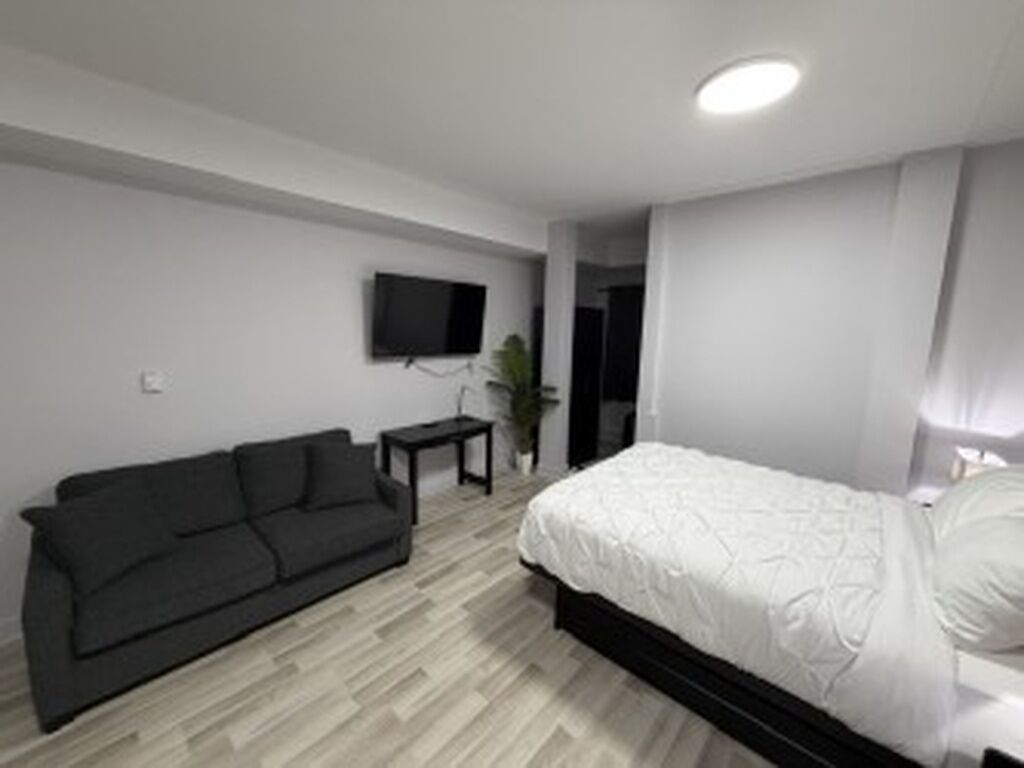 A modern bedroom with a bed, a dark sofa, a small table, and a TV mounted on the wall.