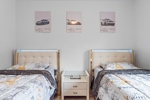 A hotel room with two beds, a nightstand, and three framed pictures of cars on the wall.