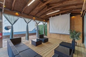 An outdoor seating area with wicker furniture, a projector screen, and a potted plant.