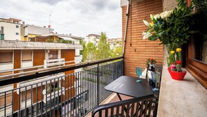 Un balcon avec une table et des chaises, un pot de fleurs, et une vue sur les bâtiments environnants.