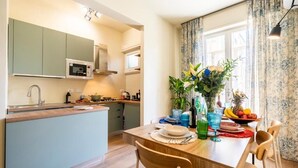 Une cuisine moderne dotée d’un îlot central, d’un coin repas avec une table dressée pour deux personnes et d’une fenêtre agrémentée de rideaux.