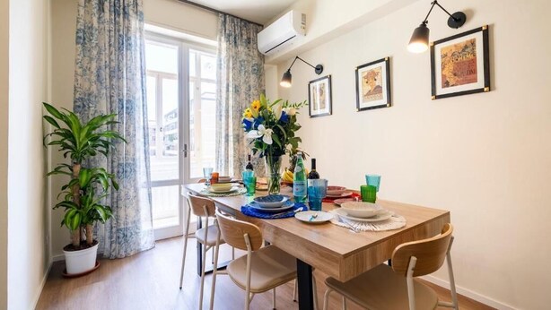 Un coin repas avec une table en bois, des chaises, une plante en pot, un vase de fleurs et des tableaux encadrés au mur.