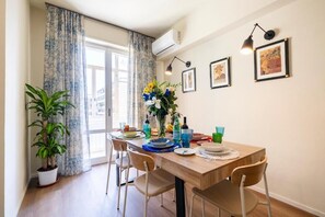 En matplats med ett träbord, stolar, en krukväxt, en vas med blommor och inramade tavlor på väggen.
