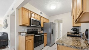 Uma cozinha moderna com armários de madeira, eletrodomésticos de aço inoxidável, bancadas de granito e piso ladrilhado.