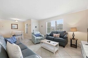 A living room with a grey sofa, a blue armchair, a wooden coffee table, and a grey sofa with a patterned cushion. - Fair Seas Clipper - Pet Friendly and Near Beach (St. Augustine Beach)