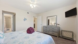 Quarto com cama, cômoda, espelho e ventilador de teto.