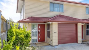 Un immeuble résidentiel de deux étages avec une porte de garage rouge, un revêtement de couleur beige et un petit porche à l’avant.