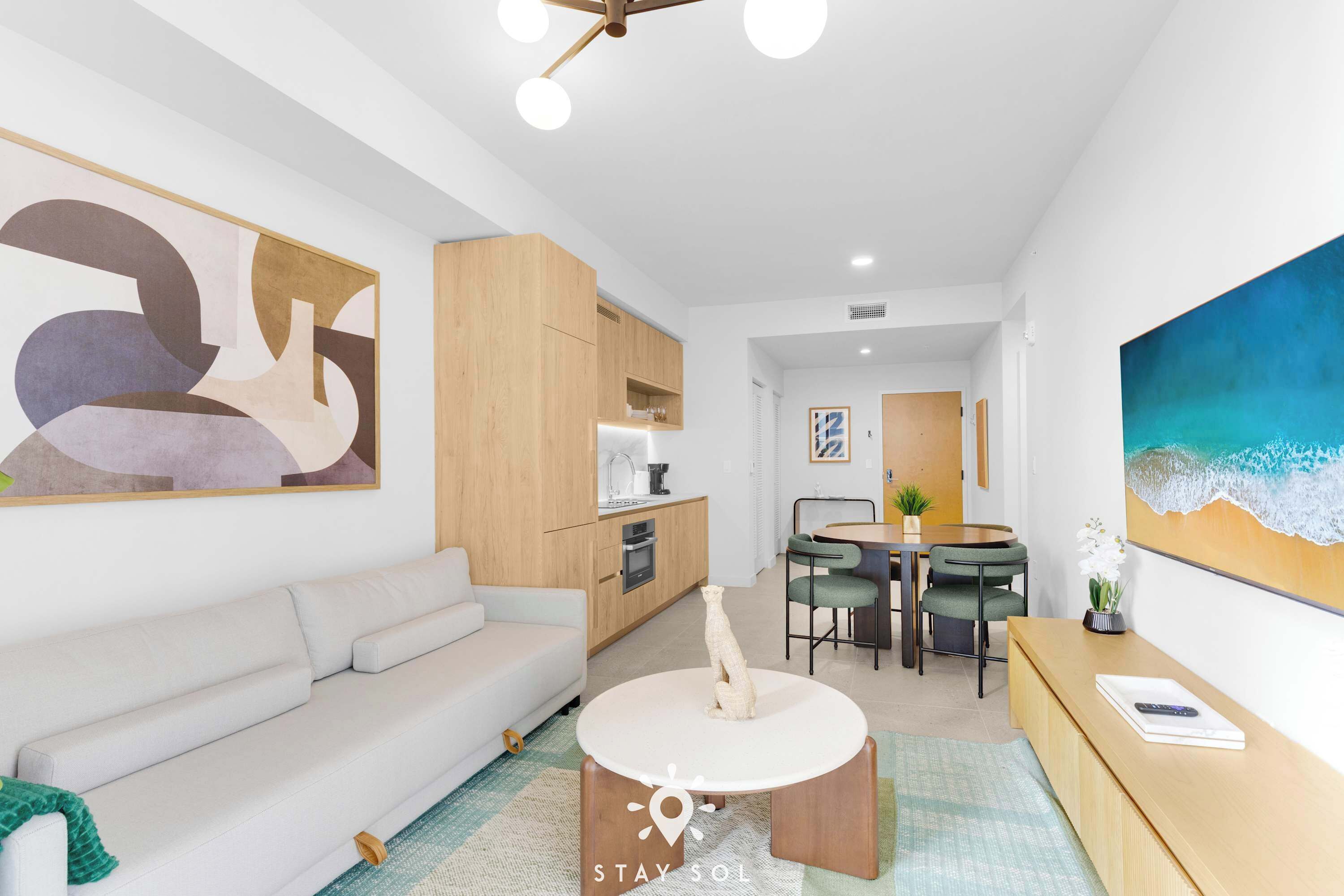 A modern living room with a sofa, a dining table with chairs, a kitchen area, and a large abstract painting on the wall.