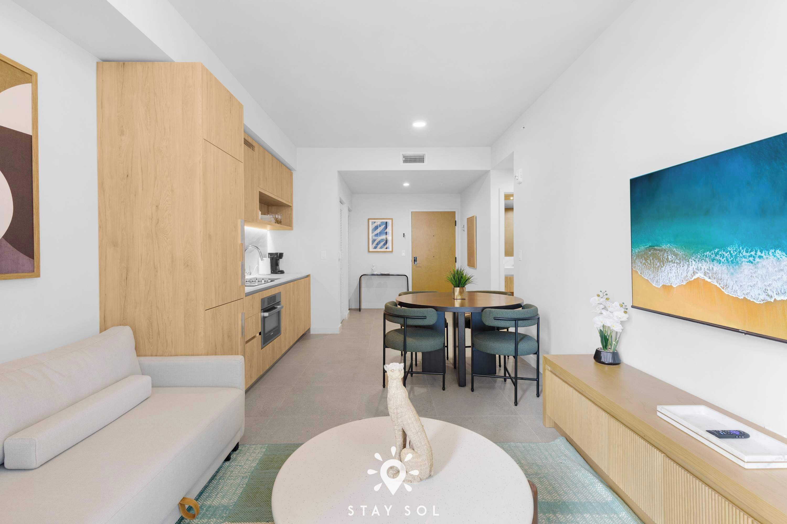 A modern living room with a sofa, a dining area with a table and chairs, a kitchen area, and a large painting on the wall.