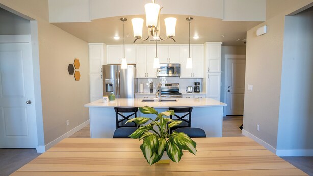 A modern kitchen with white cabinets, stainless steel appliances, and a central island with bar stools. - Escape to the heart of Colorado! (Loveland)
