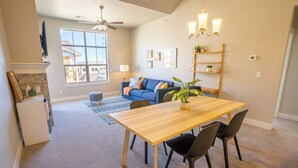 A modern living room with a dining table, chairs, a blue sofa, a ceiling fan, and a large window. - Escape to the heart of Colorado! (Loveland)