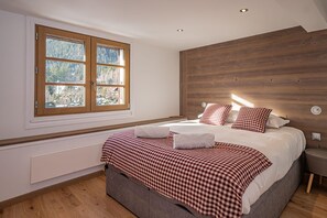 A bedroom with a large bed, wooden headboard, and a window with a view of trees. - Toits des Pècles – Stylish Alpine Loft with Mont Blanc Views (Chamonix-Mont-Blanc)