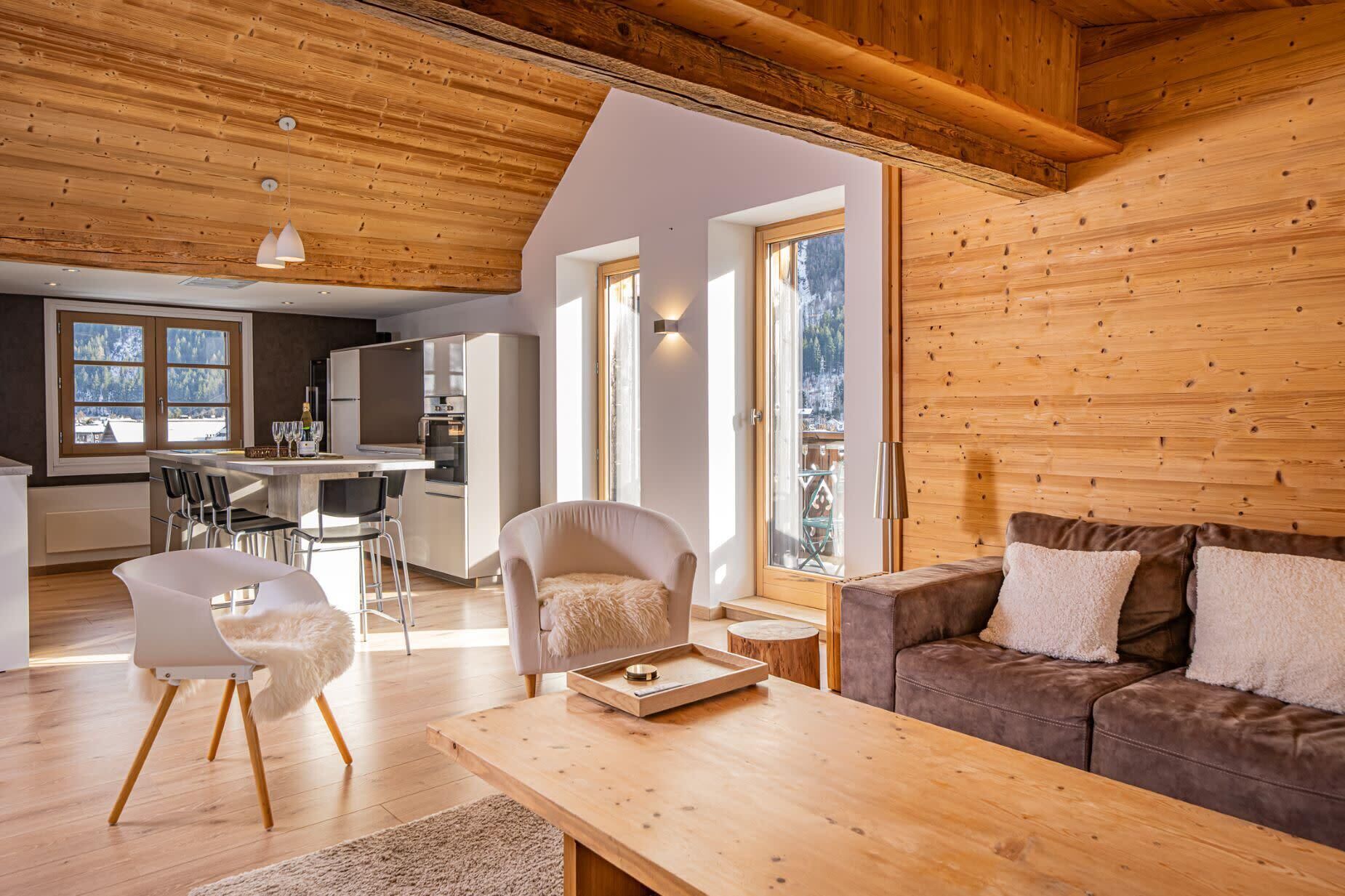 Un salon chaleureux avec un plafond en bois, un canapé marron, un fauteuil blanc et une table basse en bois.