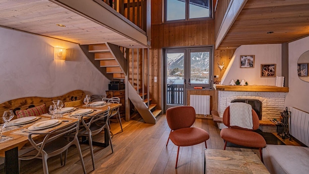 A dining area with a wooden table set for four, a sofa, and a fireplace. - Balcons de Champraz- Spectacular Mont Blanc and Lake Views (Chamonix-Mont-Blanc)
