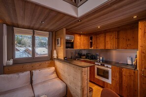 Ein gemütliches Blockhaus-Interieur mit Holzausstattung, einer Couch, einer Küche mit Holzausziehschränken und einem Fenster mit Blick auf Schnee.