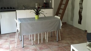 A compact kitchen with white cabinets, a small dining table with chairs, a potted plant, and a wooden ladder against the wall. - Gîte des Lavandes (MONTAGNAC MONTPEZAT)