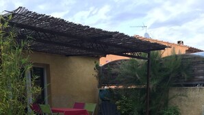 A patio with a wooden deck, a table with chairs, and a pergola. - Gîte des Lavandes (MONTAGNAC MONTPEZAT)