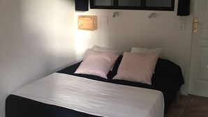 A bedroom with a bed, two bedside tables, a window with curtains, and a wall-mounted light. - Gîte des Lavandes (MONTAGNAC MONTPEZAT)