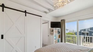 Een slaapkamer met een groot bed, een schuifdeur in Amerikaanse boerderijstijl, een televisie en een balkon met uitzicht op huizen.