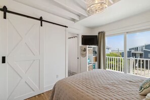 Ein Schlafzimmer mit einem großen Bett, einer Schiebetür im Scheunenstil, einem Fernseher und einem Balkon mit Blick auf Häuser.