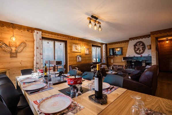 A wooden interior with a dining table set for four, a fireplace, and a television mounted on the wall.
