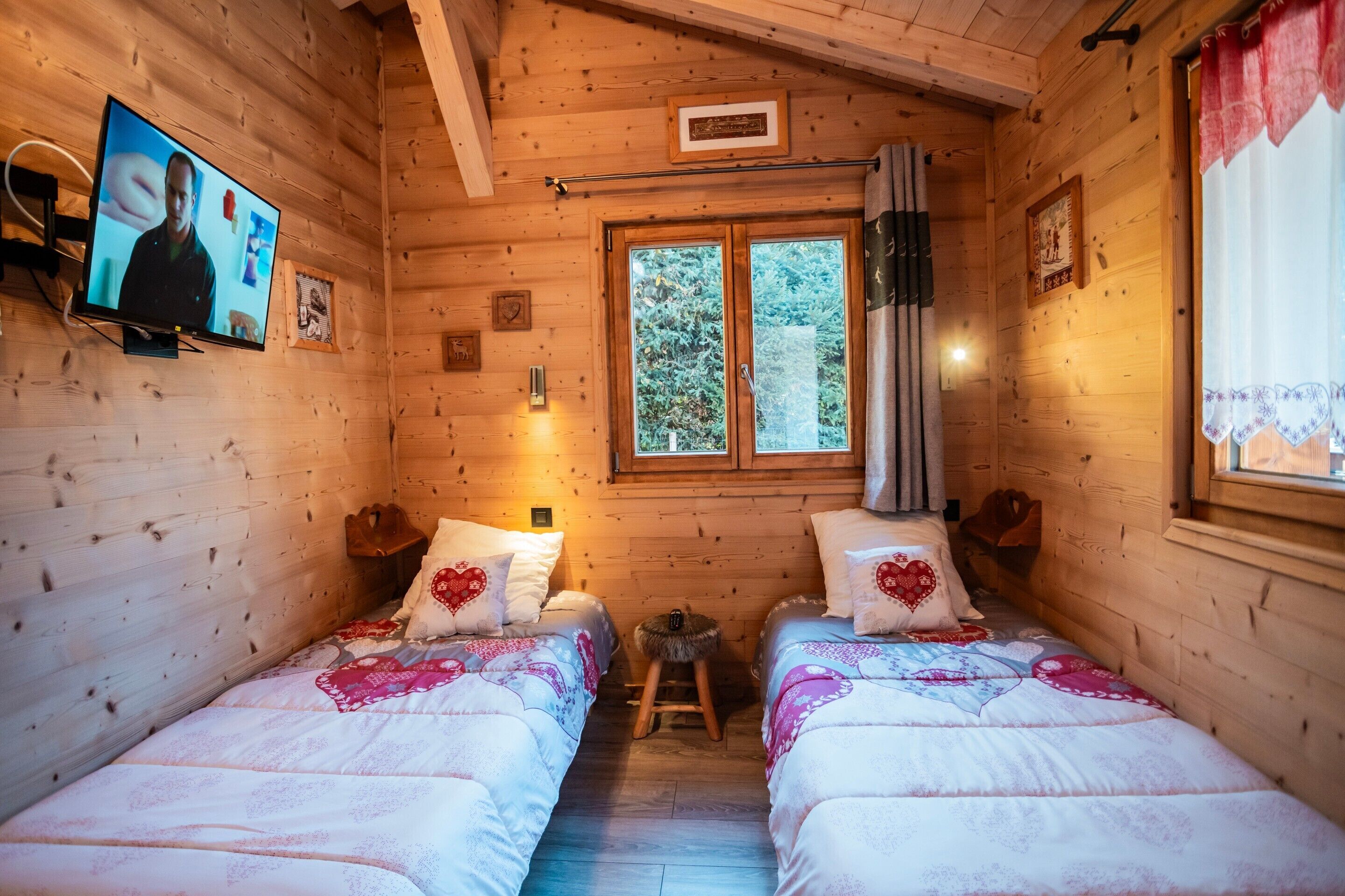 Una habitación de cabaña de madera con dos camas, un televisor y una ventana con cortinas.