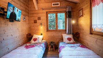 Una habitación de cabaña de madera con dos camas, un televisor y una ventana con cortinas.