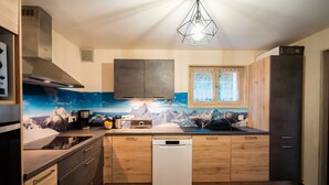 A modern kitchen with wooden cabinets, a dishwasher, and a large window. - Jacuzzi in the Heart of the Village – “L'Ours” Apartment with Private Terrace and Wi-Fi (Châtel)