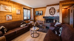 A cozy living room with a fireplace, wooden walls, and a television. - Jacuzzi in the Heart of the Village – “L'Ours” Apartment with Private Terrace and Wi-Fi (Châtel)