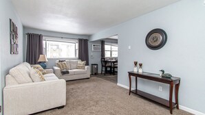 A living room with a sofa, a coffee table, and a dining area in the background. - 2BR I 4 mins to FargoDome, Free Pking, Queen x 2 (Fargo)