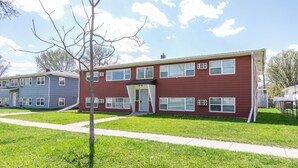 A two-story apartment building with a red exterior, multiple windows, and a small front porch. - 2BR I 4 mins to FargoDome, Free Pking, Queen x 2 (Fargo)