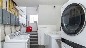 A laundry room with stacked washers and dryers, a red broom, and electrical panels on the wall. - 2BR I 4 mins to FargoDome, Free Pking, Queen x 2 (Fargo)