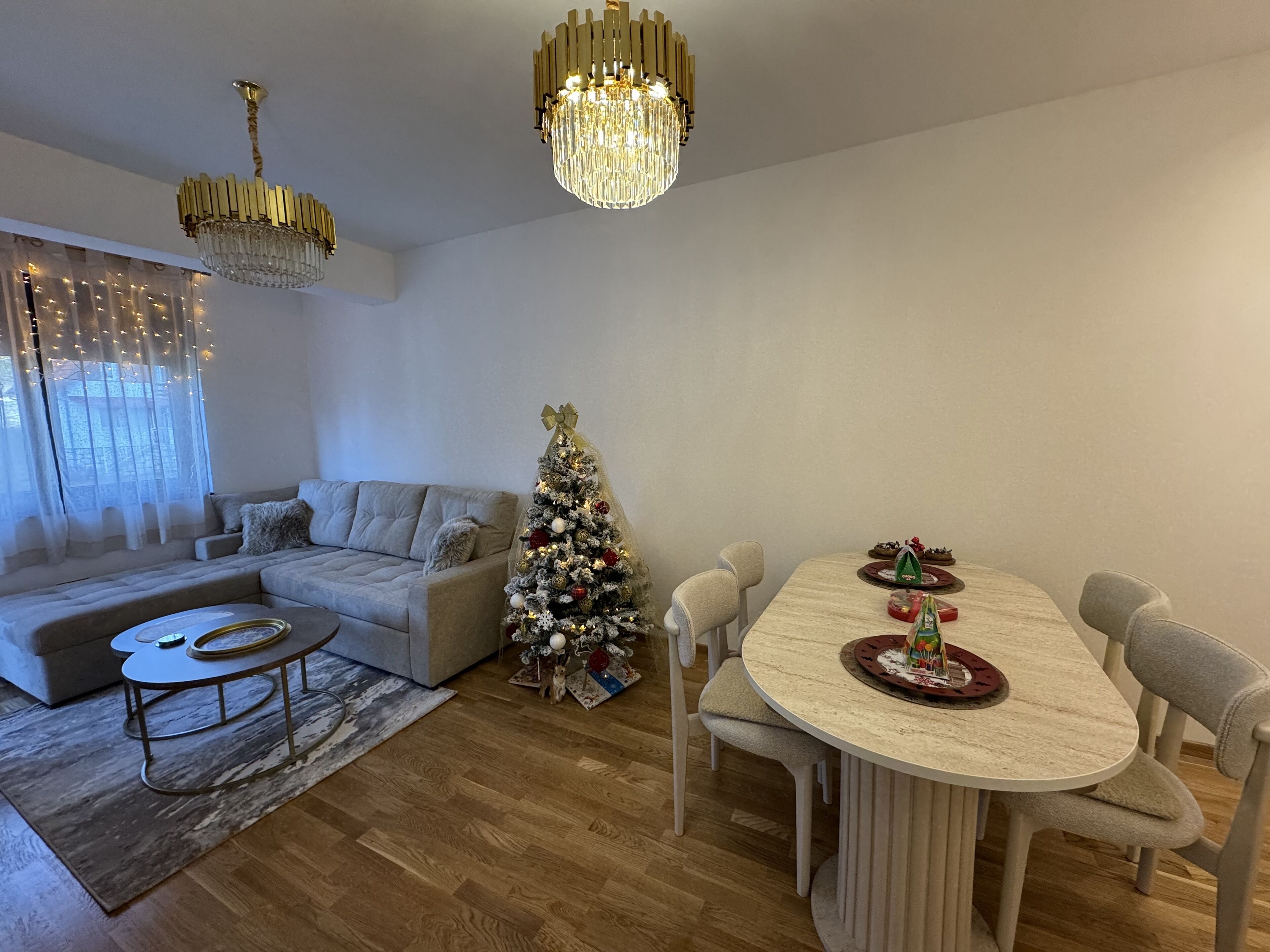 Un salon moderne avec un canapé, une table à manger et des chaises, un sapin de Noël et deux lustres.