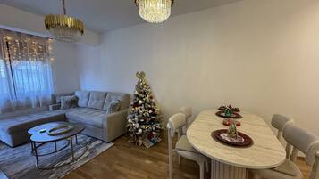 Un salon moderne avec un canapé, une table à manger et des chaises, un sapin de Noël et deux lustres.