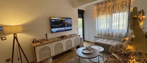 Un salon moderne avec un téléviseur, un lustre, un sapin de Noël et un coin salon confortable.