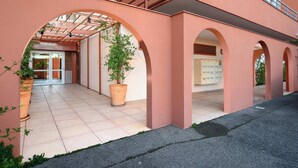 A building with a covered entrance area, potted plants, and a tiled floor. - Le Panama (Saint-Raphaël)