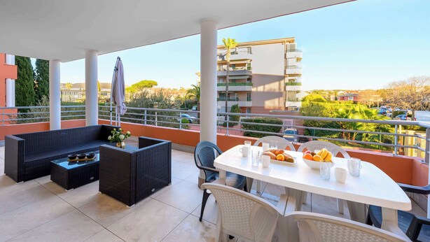 A balcony with a white table set for breakfast, wicker furniture, and a view of the cityscape. - Le Panama (Saint-Raphaël)