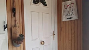 Una puerta blanca con un pequeño ventanal, un pomo de latón y una pared de madera.