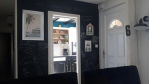 Una habitación con una pared oscura, una puerta blanca y una zona de cocina visible con una cafetera.