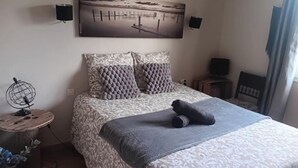 Un dormitorio con cama, una obra de arte en la pared, una mesita con un globo terráqueo y un televisor sobre un soporte.