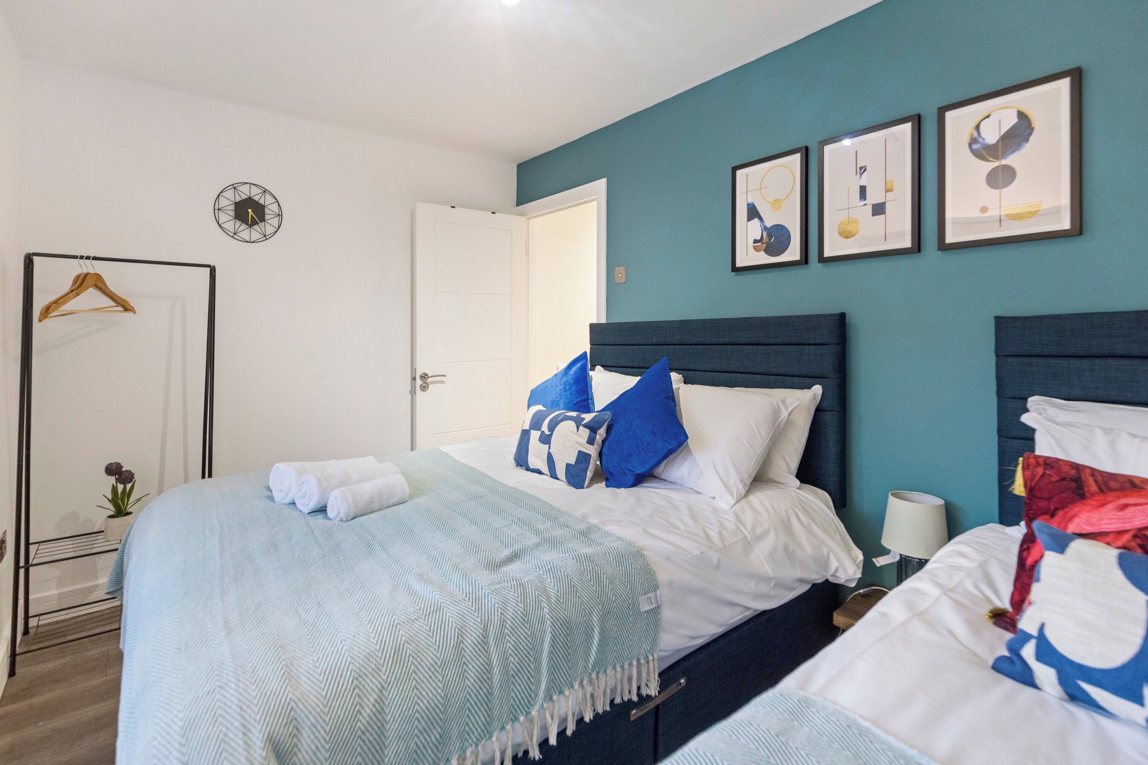 A bedroom with a bed, a bedside table, a lamp, and a wall clock.