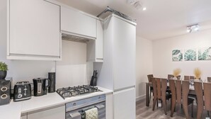 Uma cozinha moderna com armários brancos, fogão a gás e uma área de refeições com cadeiras e mesa de madeira.