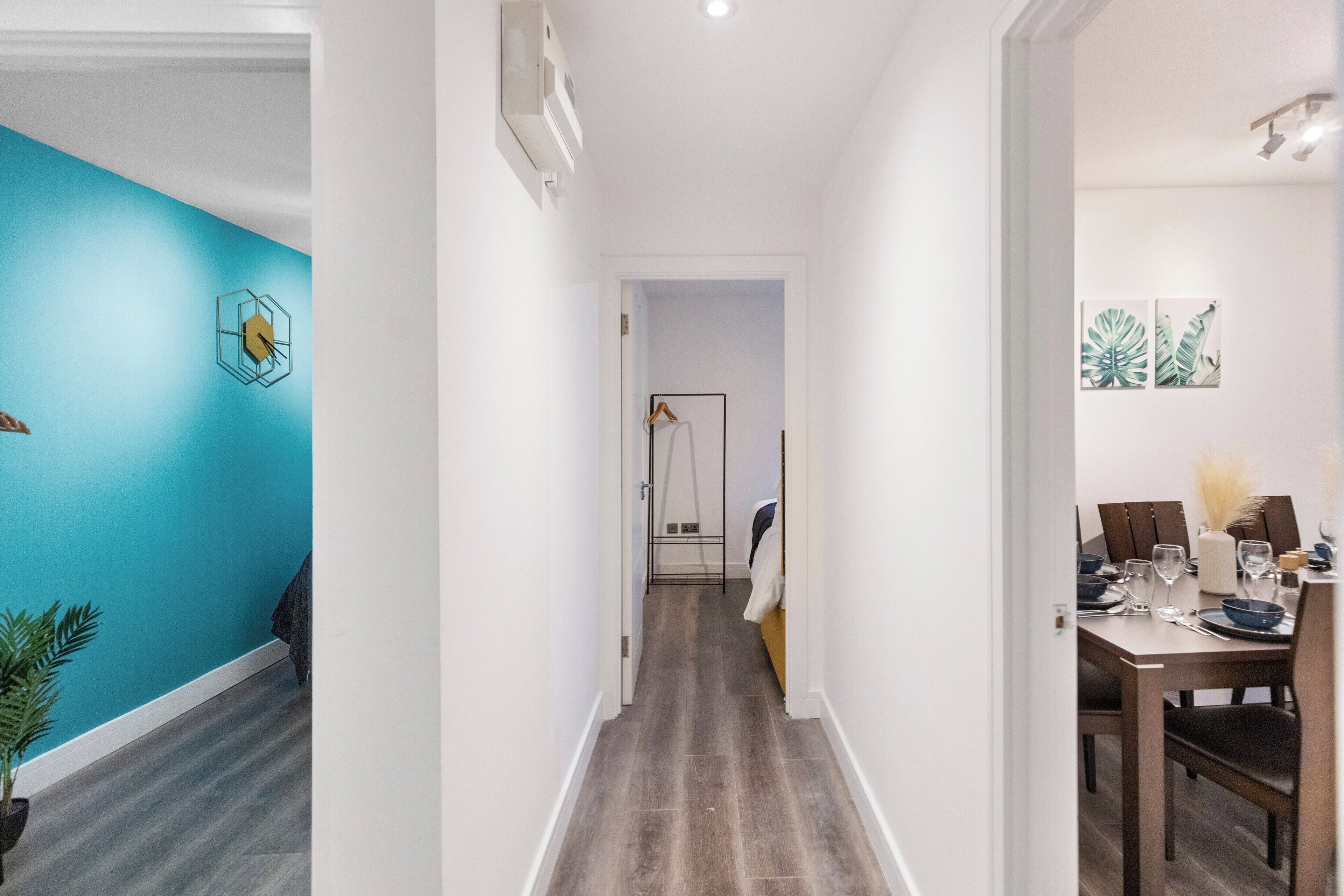A hallway with a blue wall, a dining area with a table set for four, and a door leading to another room.
