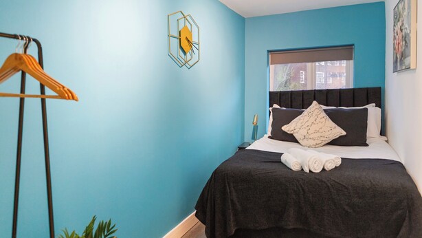 Quarto com uma cama, janela, relógio na parede e planta.