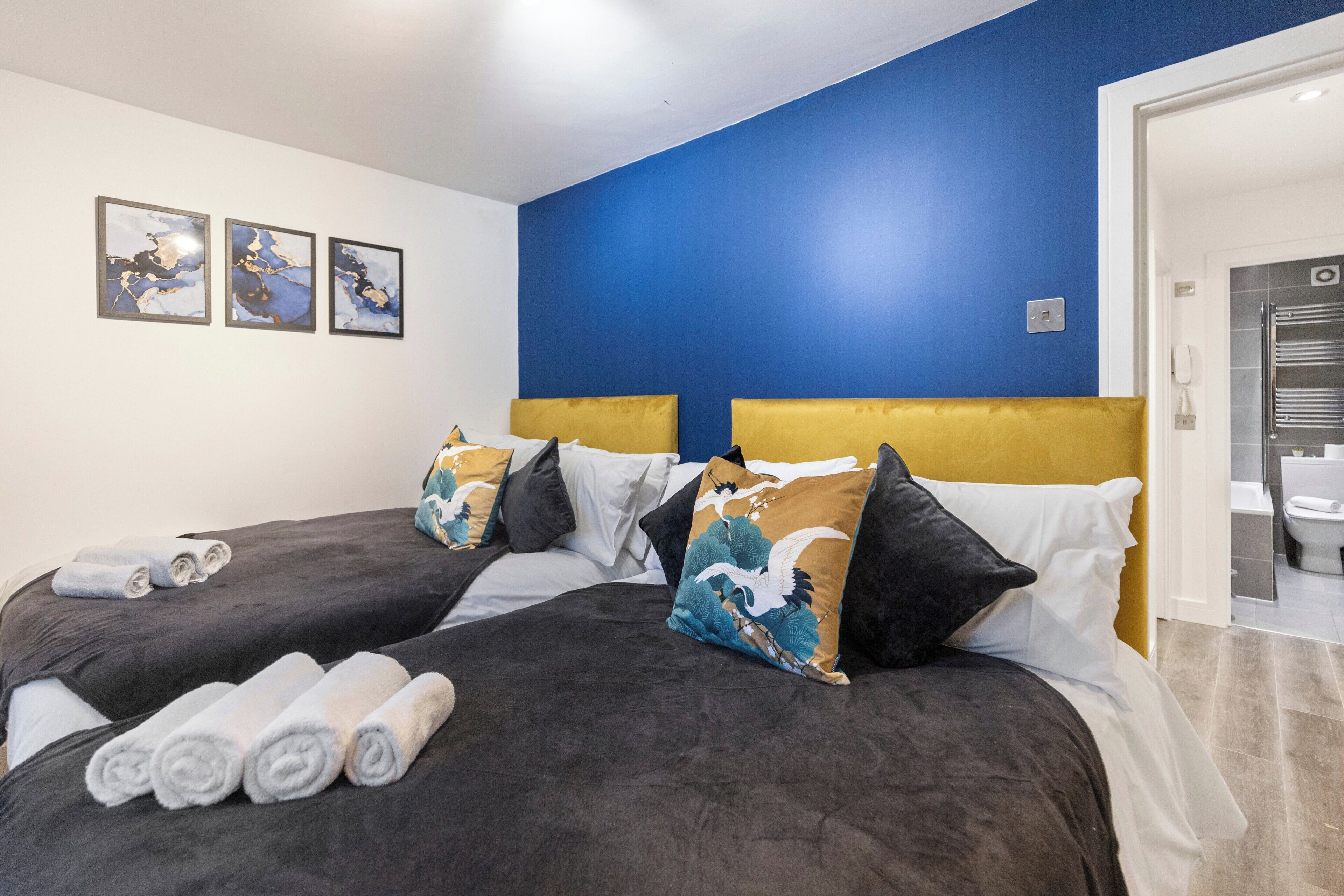 A hotel room with two beds, dark bedding, and a blue accent wall.