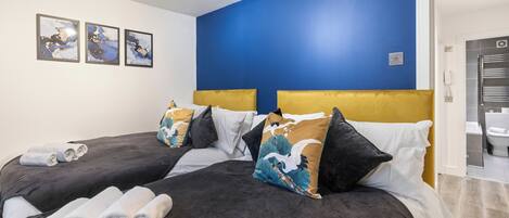 A hotel room with two beds, dark bedding, and a blue accent wall.