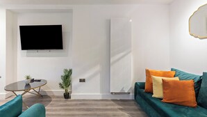 Uma sala de estar moderna com uma TV de tela plana, uma mesa de vidro redonda, sofás verde-água e um radiador branco.