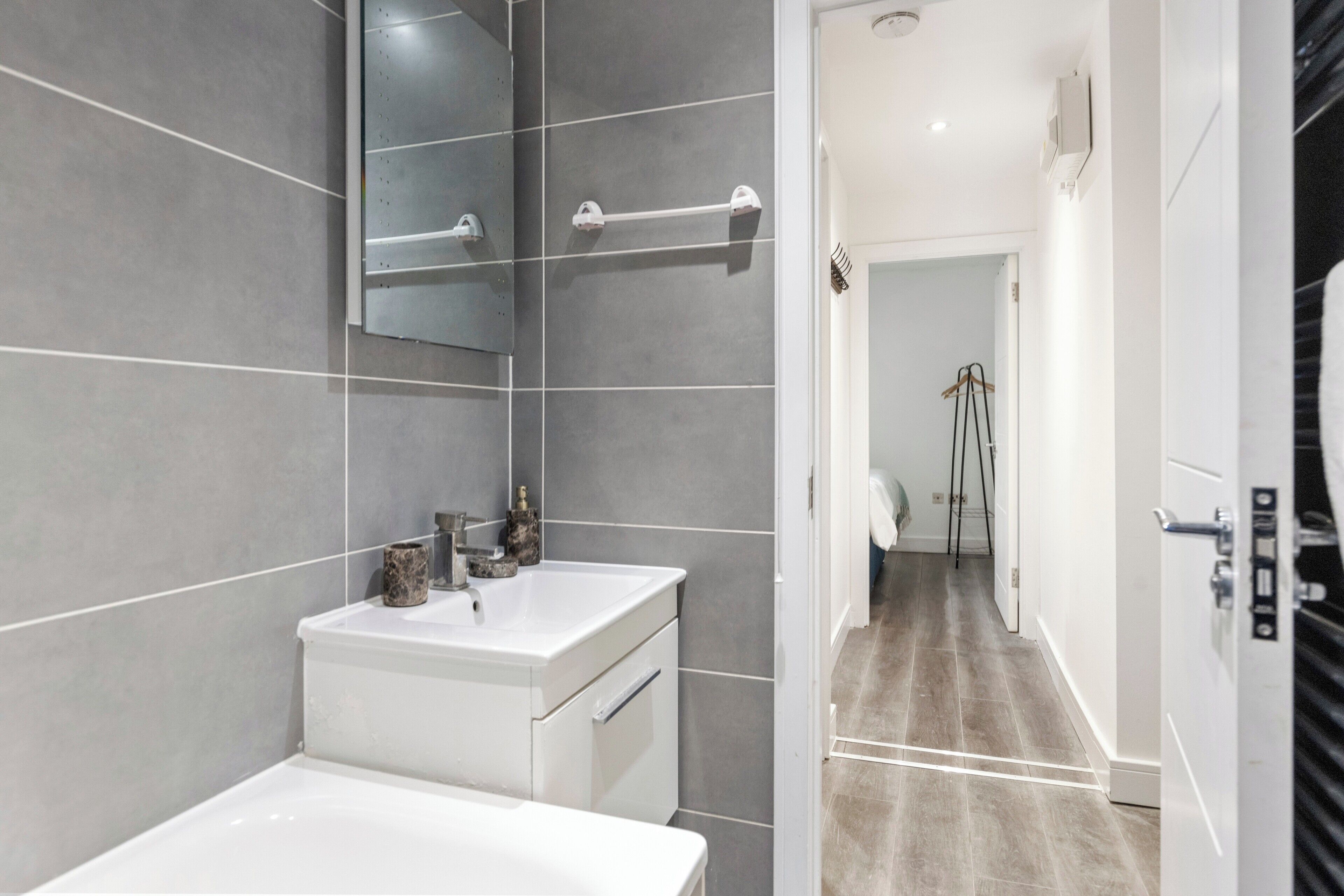 A modern bathroom with a white sink, mirror, and towel rack.