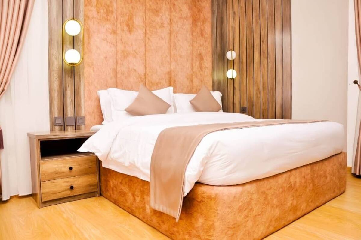 Un lit bien fait, avec une literie blanche et beige, une tête de lit en bois et des lampes de chevet.